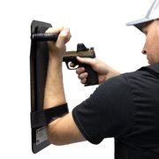 Person holding up a black 8" x 17" Caliber Armor Ballistic Shield with handle padded armrest & forearm strap while pointing a pistol 7