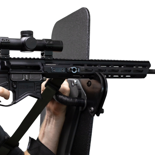 Close-up of a rifle with a scope resting on a support bracket that is mounted to a bulletproof shield 5